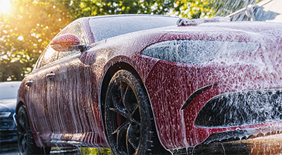 Voiture rouge en cours de lavage avec un jet d'eau &agrave; haute pression.